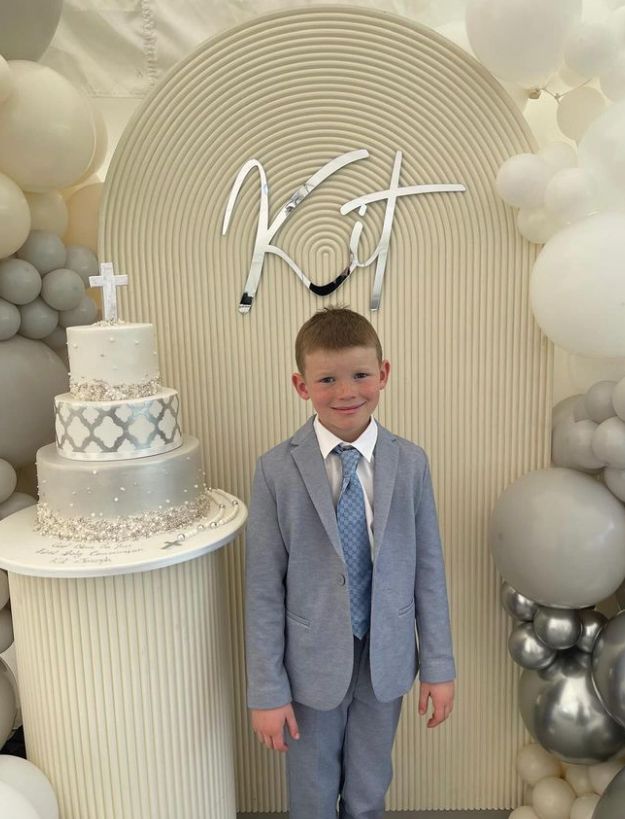 A young boy in a suit standing next to a white cake