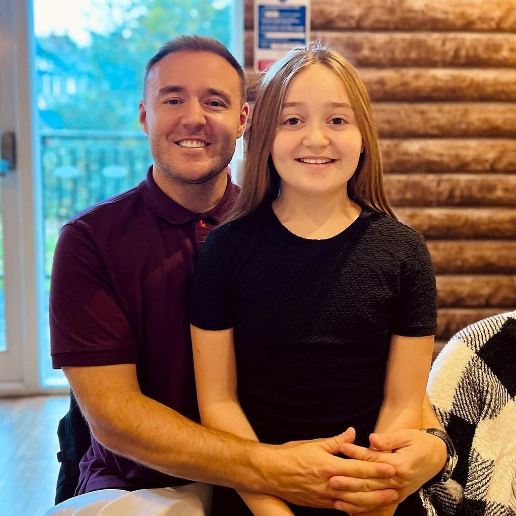 Alan Halsall in a maroon polo neck with his daughter sitting on his lap