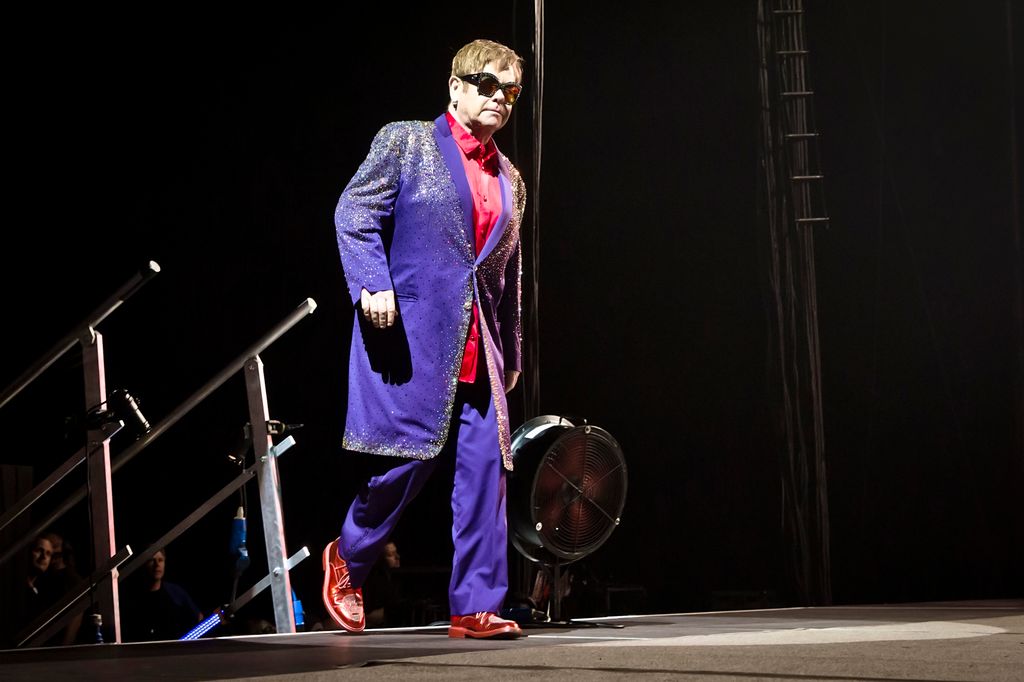 Elton John walking onto a stage in a purple and red suit