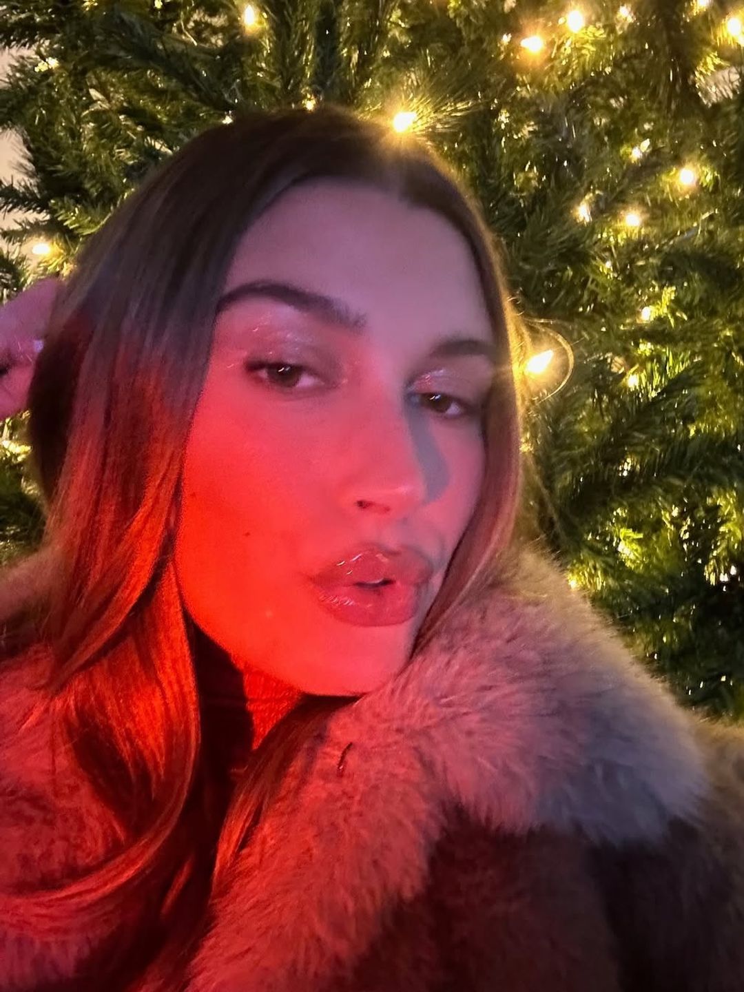 Hailey Bieber's glossy lips, radiant skin, and a faux-fur jacket paired with glowing lights showcased festive beauty with subtle drama.