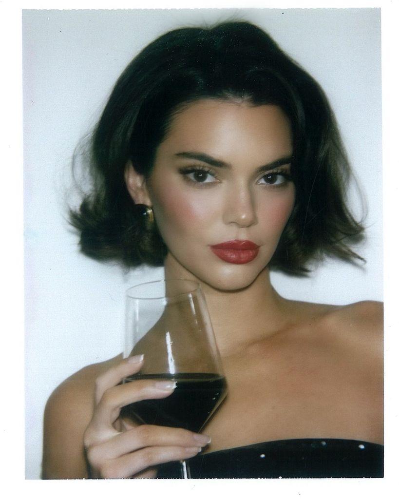 Kendall Jenner holding a glass of wine while wearing red lipstick with her hair in a bob