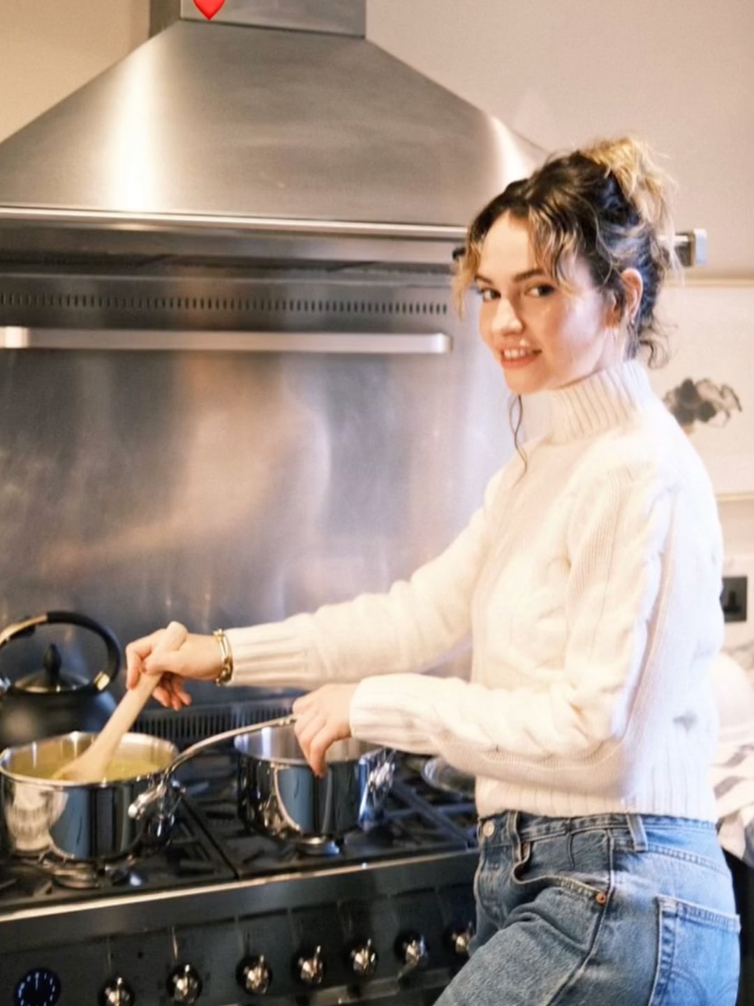 Lily James' cream cable-knit cashmere sweater and vintage jeans made cooking stylishly casual. A cheerful moment filled with holiday warmth.