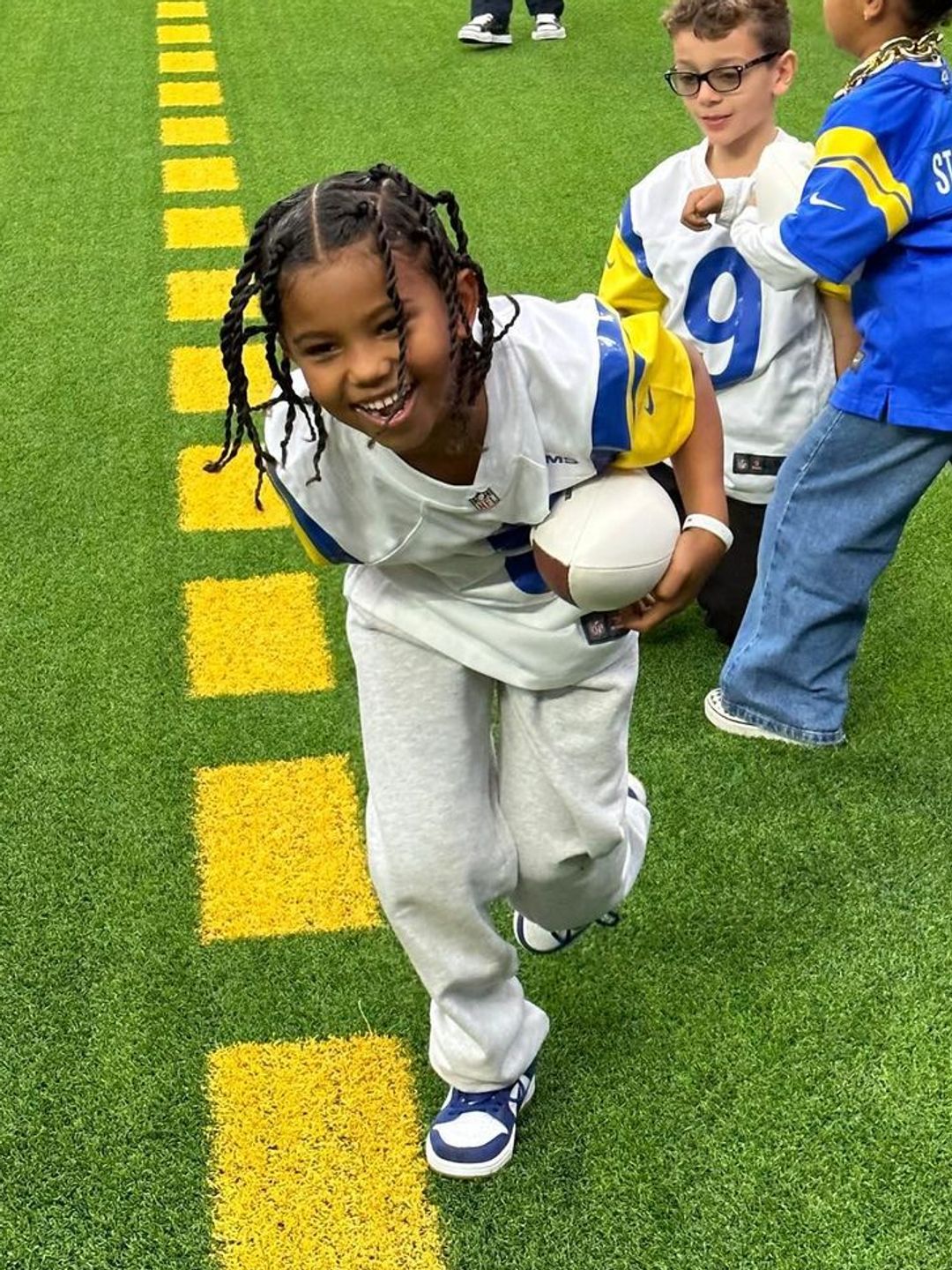 Saint running with a football on a football pitch, smiling