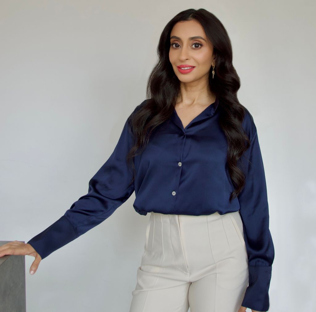 Woman standing in a silky blue shirt and white trousers