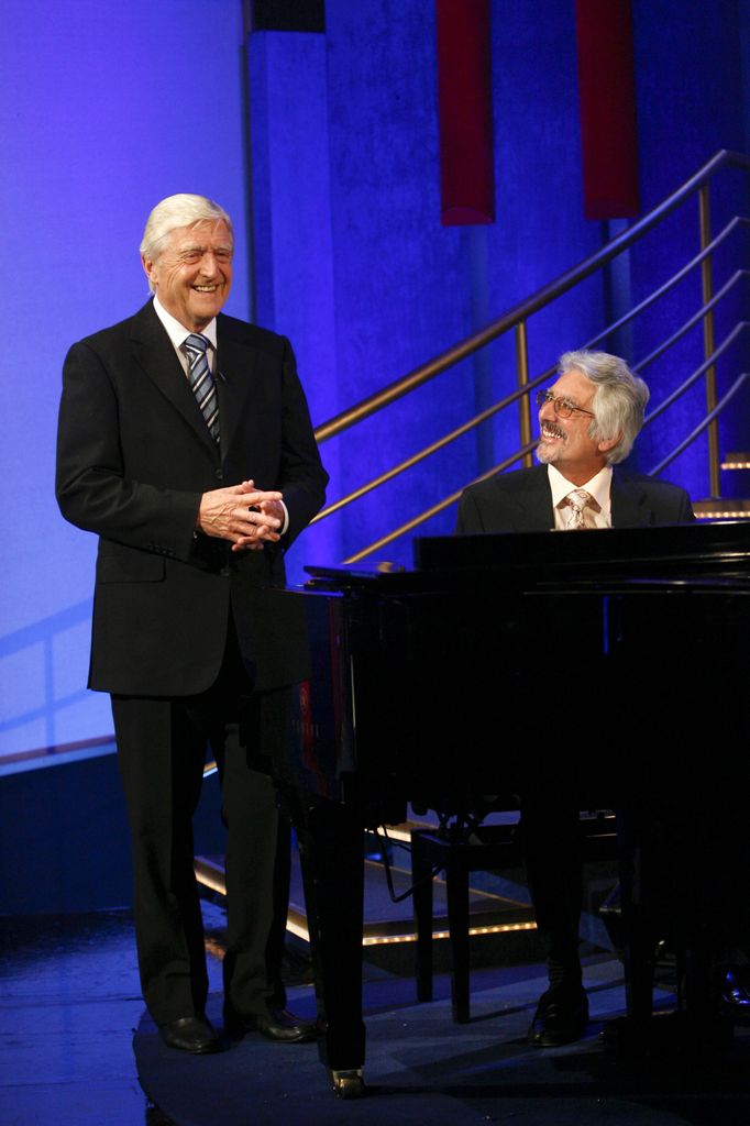 Sir Michael Parkinson standing while Laurence Holloway sits at the piano