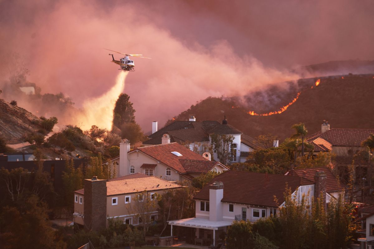 A helicopter drops water around homes threatened by the wind-driven Palisades Fire 