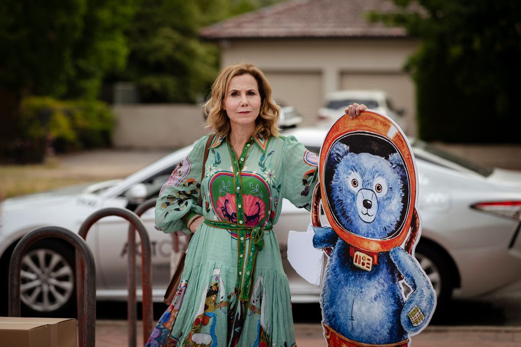 blonde woman in green dress holding bear cartoon cut-out on street