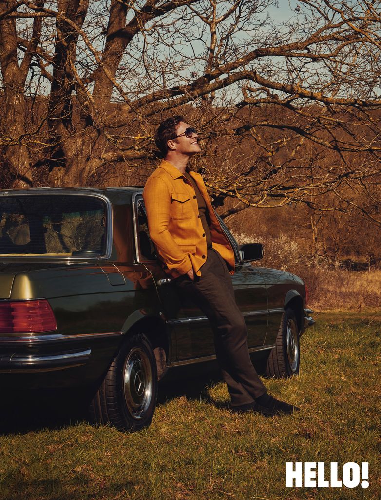 A man posing against a car with his hand in his pocket and looking towards the sky
