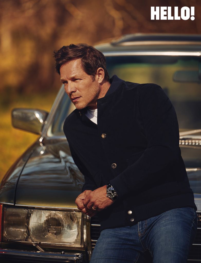 A leaned against the front of a car whilst wearing a black cardigan and blue jeans