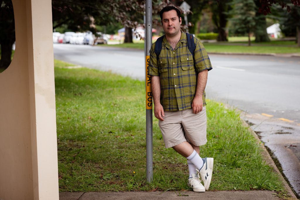 Young man in green shirt and shorts standing on grass on pavement