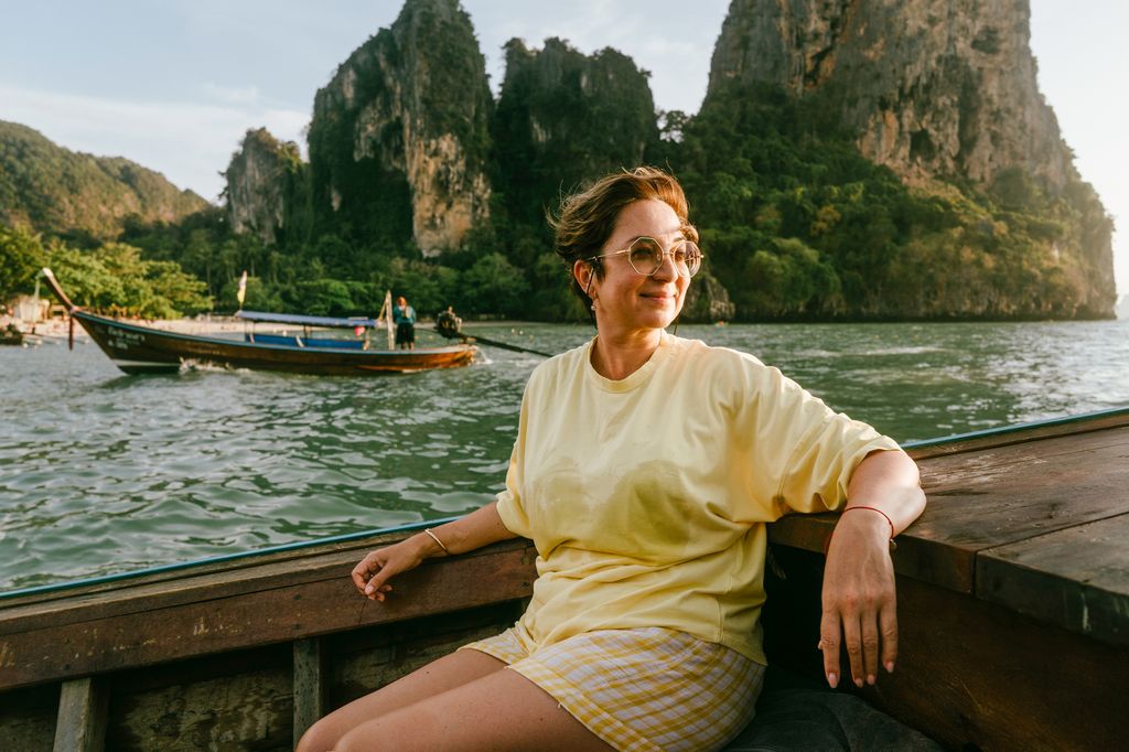 Happy beautiful woman of pre-retirement age in sunglasses and a yellow T-shirt sitting on board a wooden boat. Enjoying nature, the sea, the Phuket islands, Krabi province. Retirement age in pleasure and unity with nature, sustainability