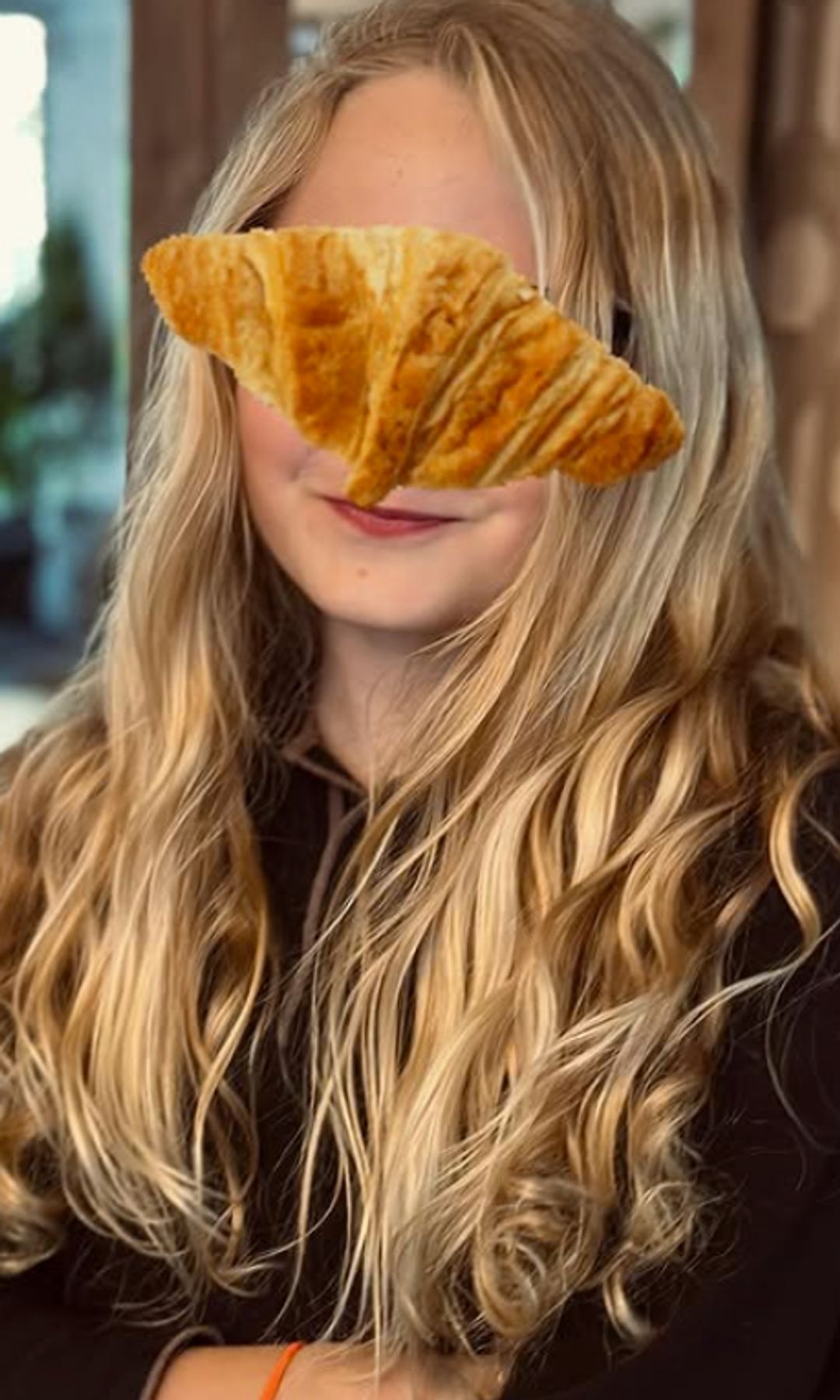 A young girl with a croissant emoji covering her face