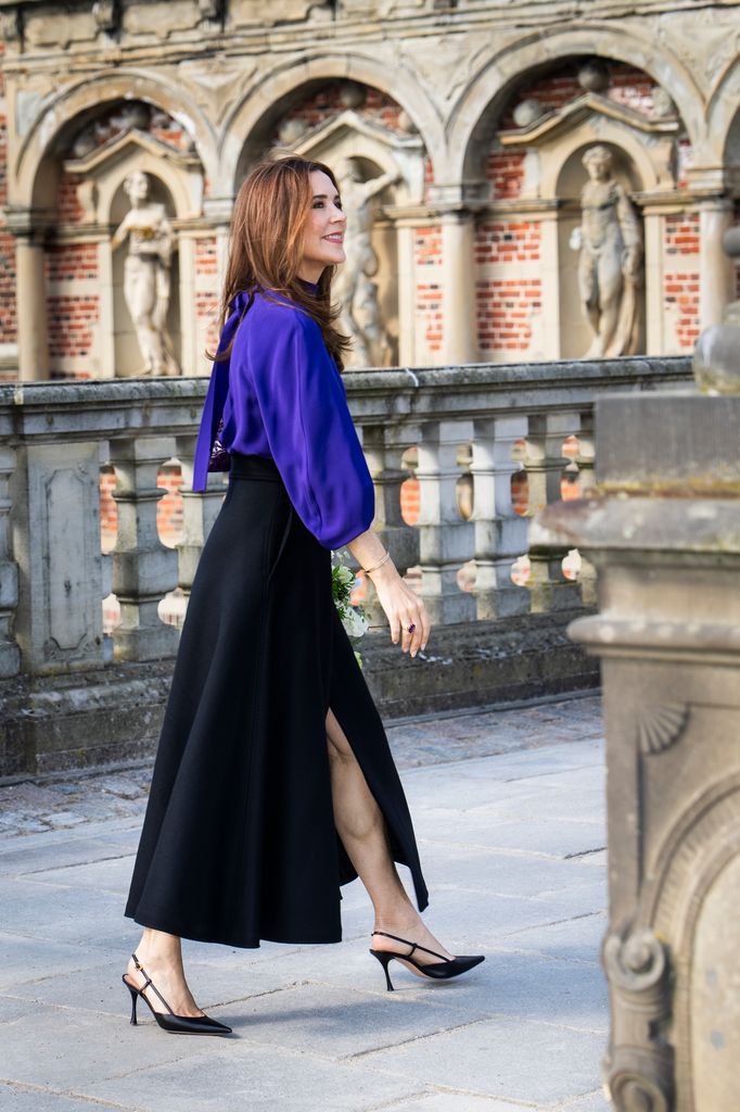 Queen Mary walking in a black skirt, blue top and black heels