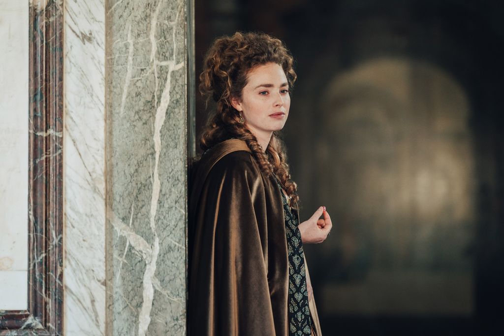 woman in period clothing standing against wall