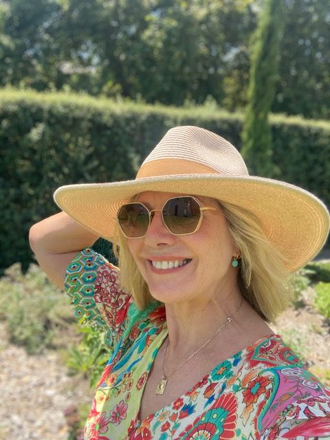 Woman smiling in a printed dress with a sun hat on 