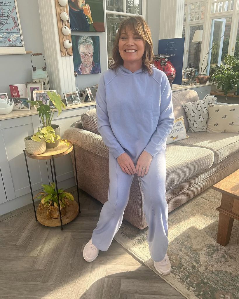 Lorraine Kelly in a purple tracksuit perched on the edge of a sofa