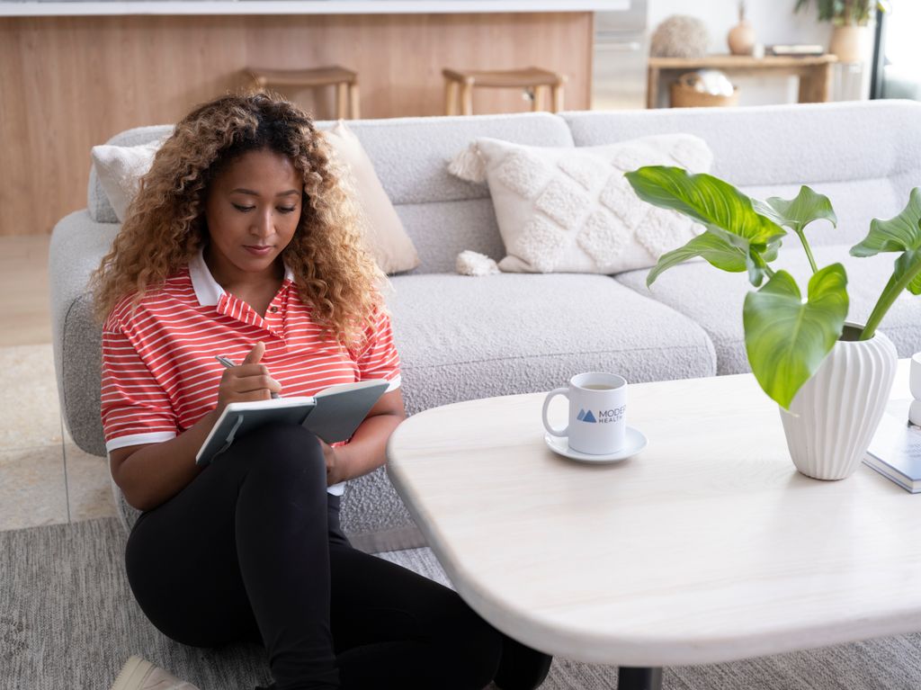 naomi osaka writing in book on floor of lounge 