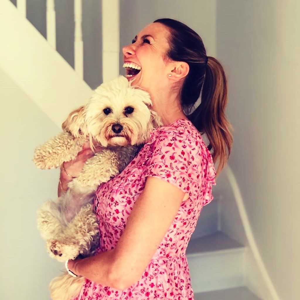 Woman laughing in a pink dress while holding a fluffy white dog
