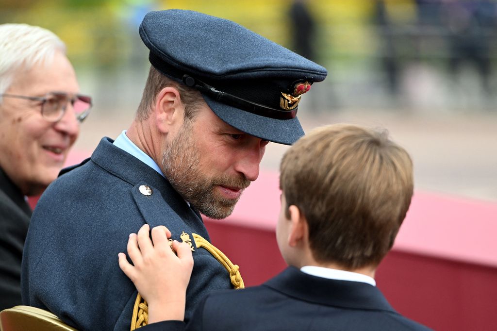Prince Louis touches his dad's uniform while they watch the military procession on The Mall