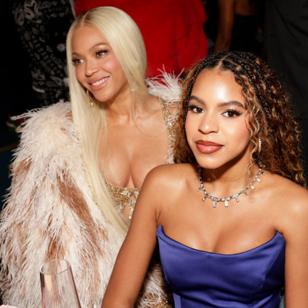 blue ivy sits in a blue dress with beyonce who is wearing white fuzzy coat