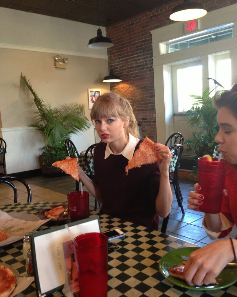Taylor Swift holds two slices of pizza in a pizzeria