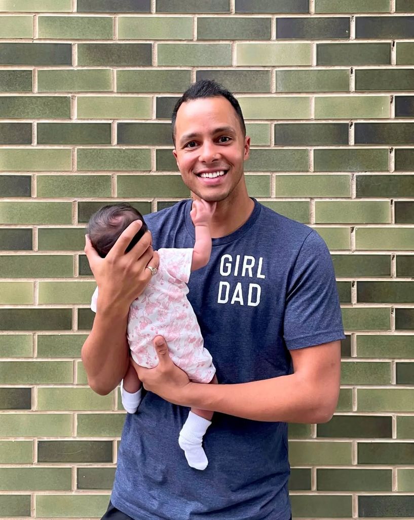 will kirk holding baby girl with green brick wall backdrop
