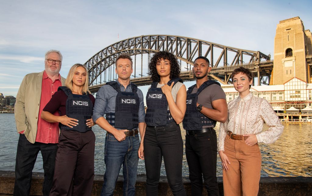 The NCIS:Sydney season 2 cast from left to right: William McInnes as Forensic Pathologist Dr. Roy Penrose, Tuuli Narkle as AFP Liaison Officer Constable Evie Cooper, Todd Lasance as AFP Liaison Officer Sergeant Jim 'JD' Dempsey, Olivia Swann as NCIS Special Agent Captain Michelle Mackey, Sean Sagar as Special Agent DeShawn Jackson, and Mavournee Hazel as Forensic Pathologist Bluebird