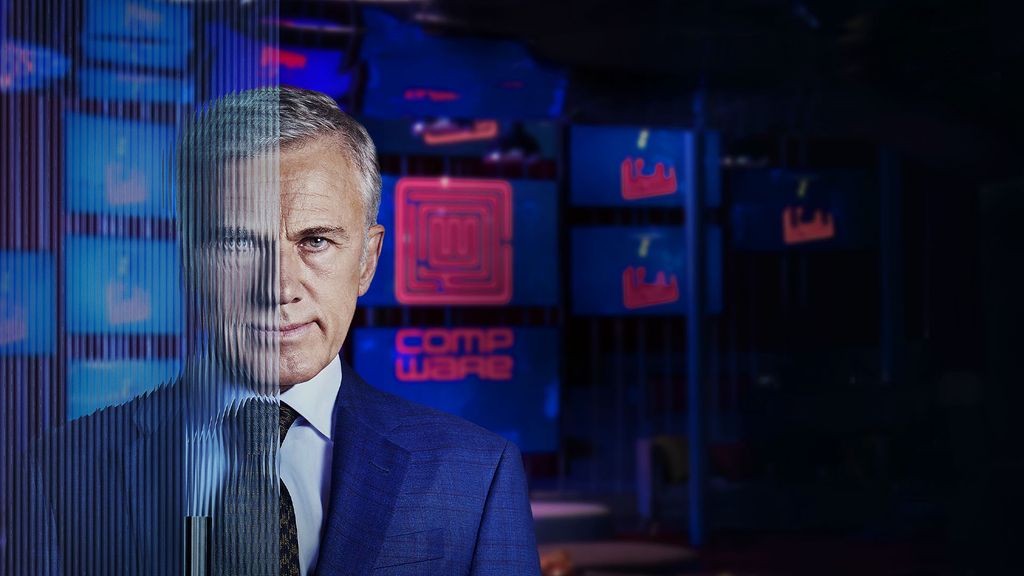 man in suit standing in front of room full of screens