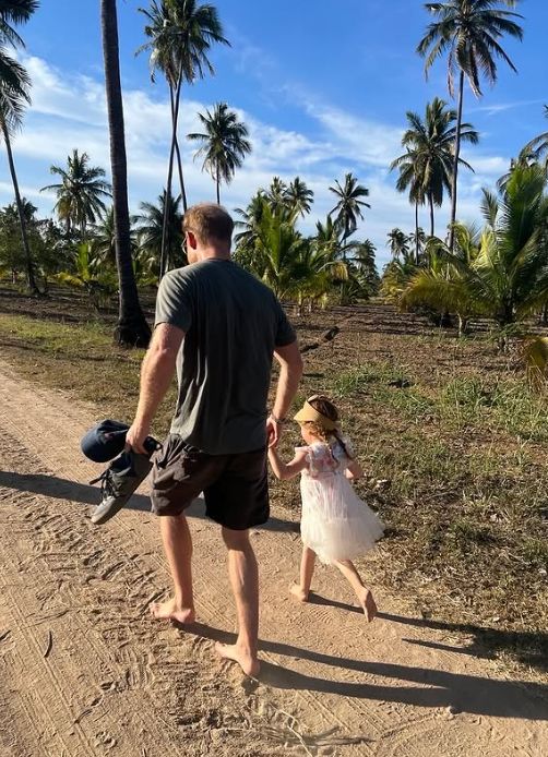 Prince Harry walking with Princess Lilibet on a sandy path