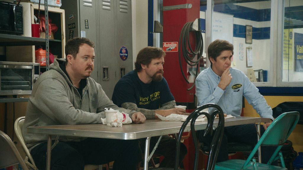 three men sitting at table in workshop