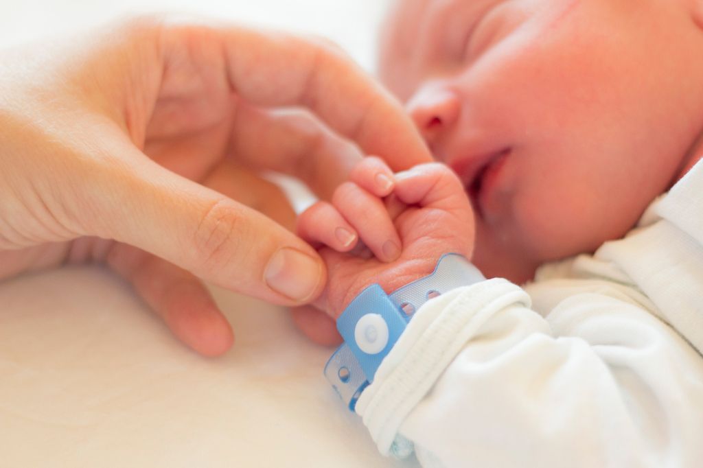 A sleeping newborn baby with his parents hand holding his
