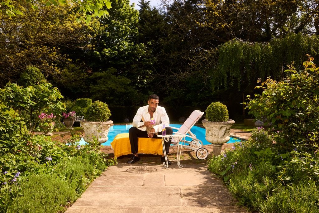 Lucien Laviscount by a pool holding a drink