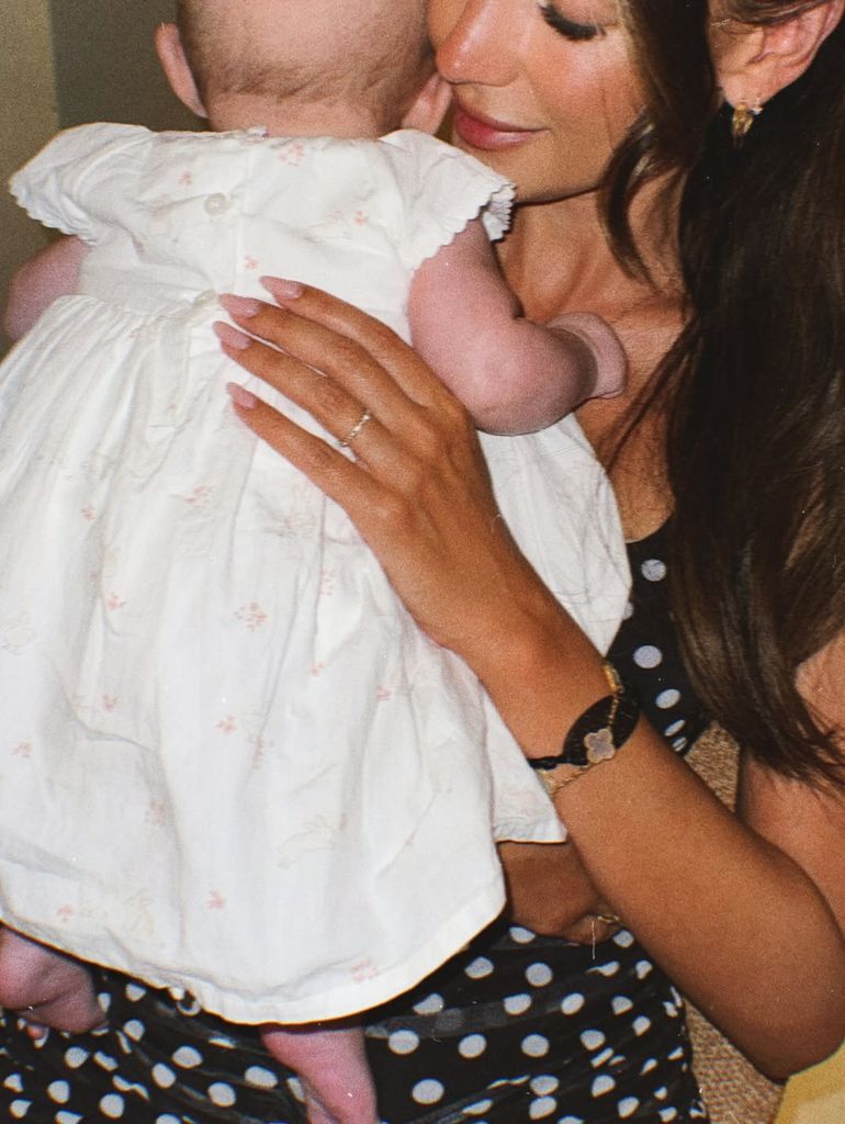 Michelle Keegan in polka dot dress holding baby Palma who is wearing white dress with pink flowers