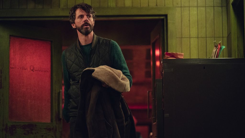 man with beard holding coat in dimly-lit room
