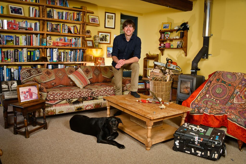 Simon Reeve sitting in his living room with yellow walls and red sofas