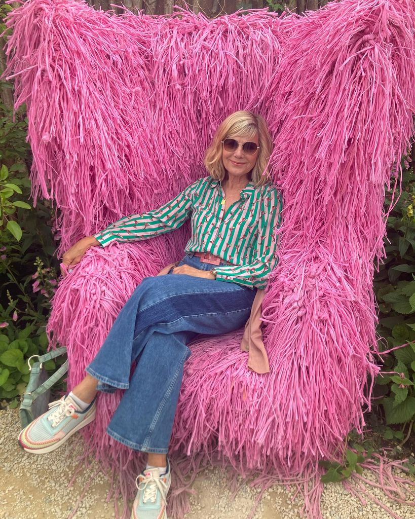 glynis barber sitting in a fluffy pink chair in jeans and a striped shirt