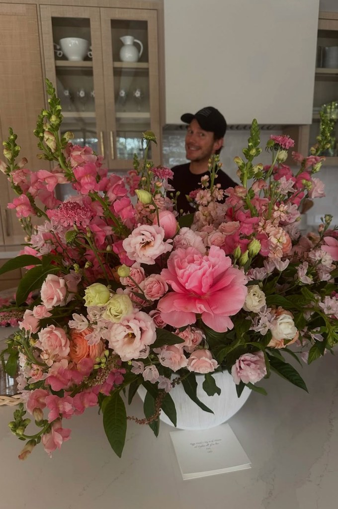 Photo shared by Katherine Schwarzenegger of a bouquet of flowers and Chris Pratt smiling behind them