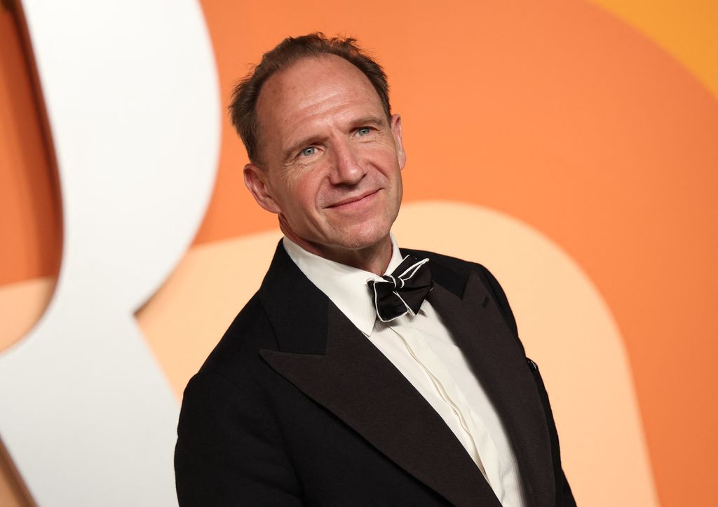 Ralph Fiennes smiling in a black suit, white shirt and bow tie at the oscars in 2025