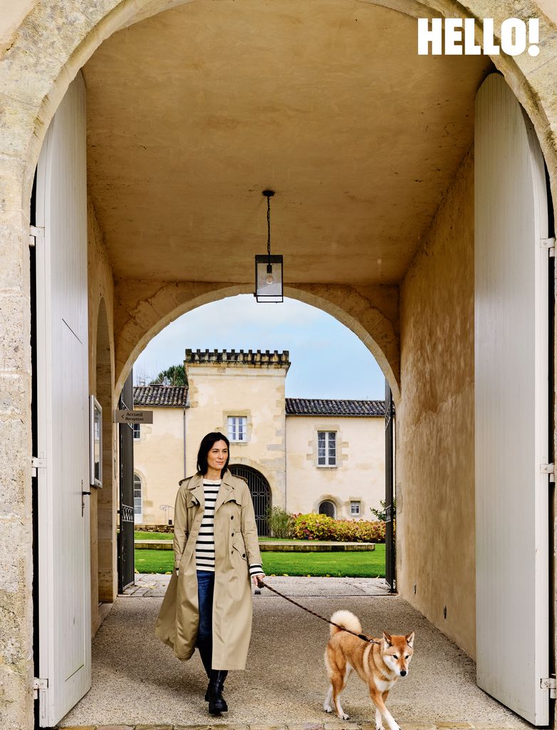 Amélie in a biege coat with her dog at the entrance to the Château Toulouse-Lautrec