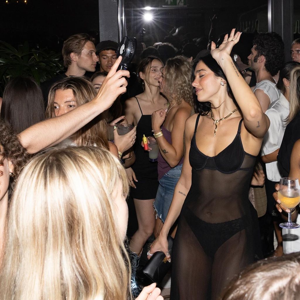 Dua Lipa dances with friends wearing a black sheer dress with black underwear underneath