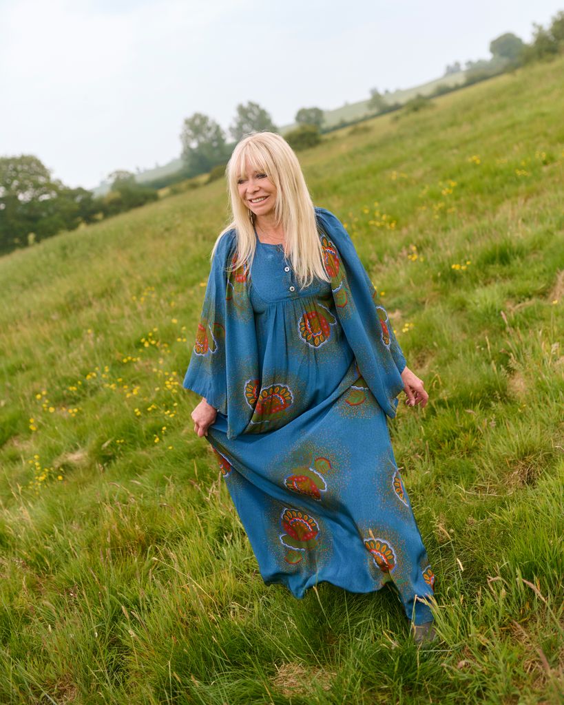 Jo Wood frolicking in a field in  a printed blue dress