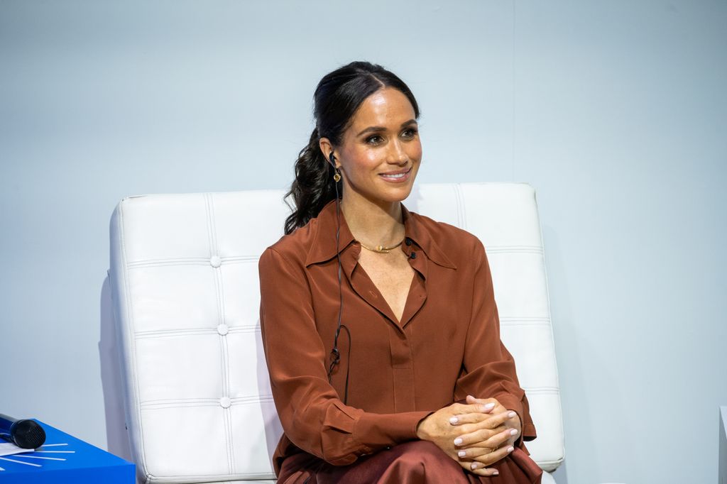 Meghan Markle wearing brown shirt sitting on speaking panel