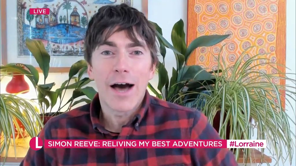 Simon Reeve in a checked shirt with plants and pictures in the background