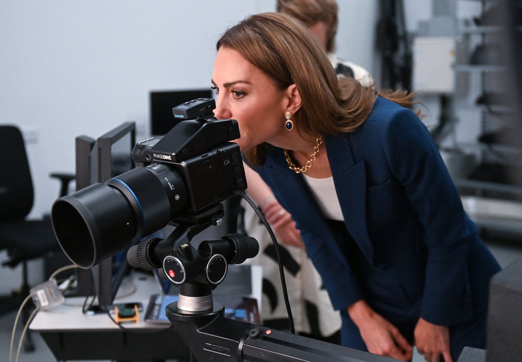 Kate Middleton in teal suit looking through viewfinder of a camera