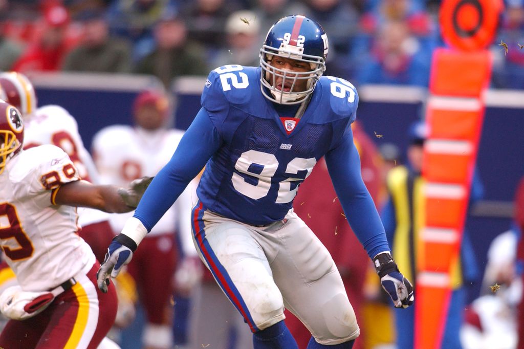 Michael Strahan plays american football wearing a helmet and full kit on the field