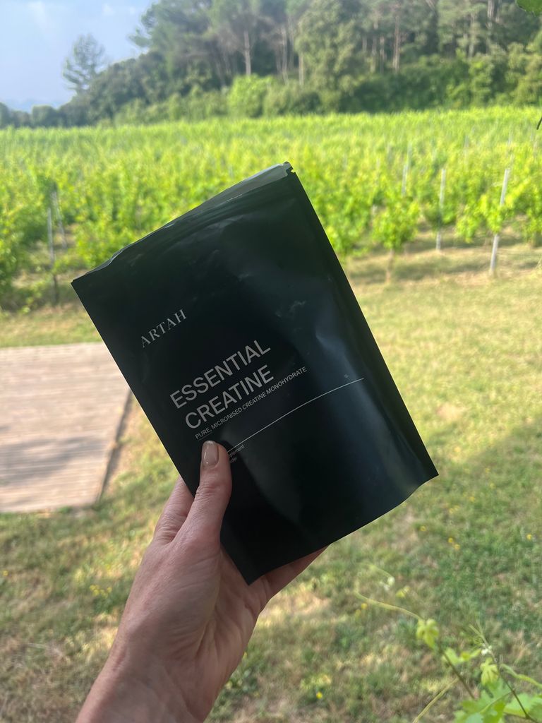 hand holding a bag of artah creatine supplements in front of a green field 