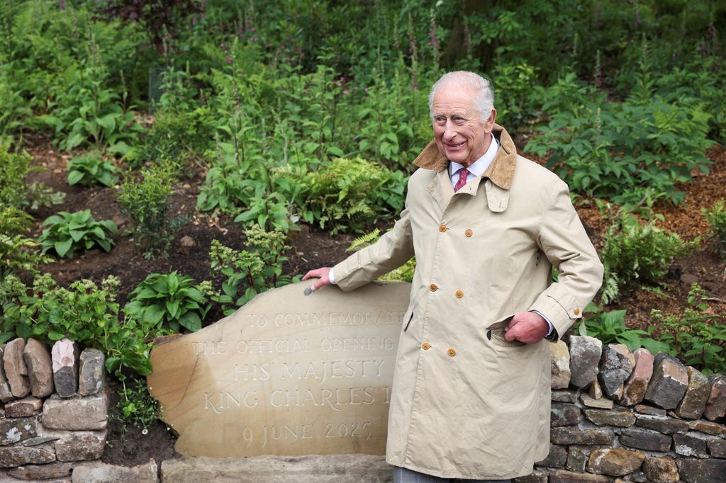 king charles in coat posing with plaque in woodland area