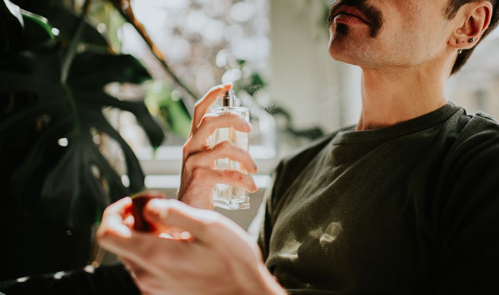 A man sprays aftershave on himself.