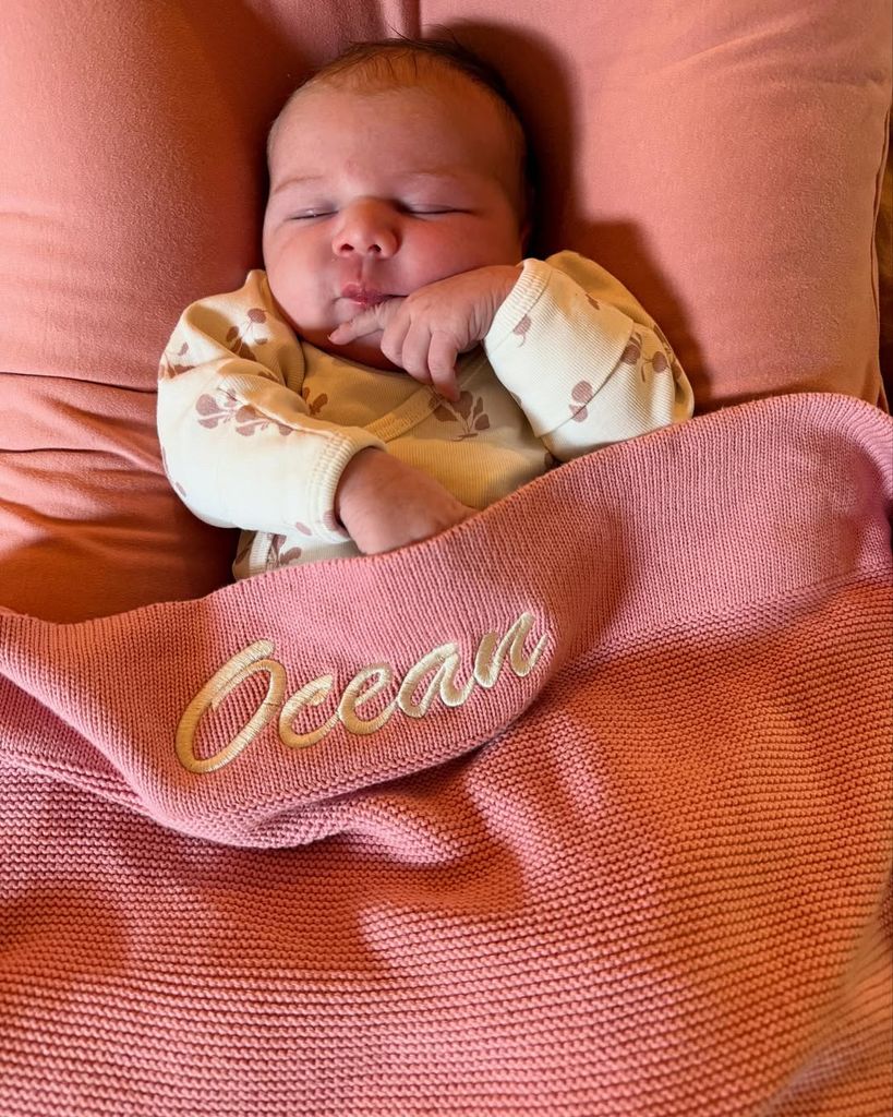 Sarah Wright Olsen and Eric Christian Olsen's newborn baby girl, Ocean Rain Olsen, lays in bed in a blanket with her monogram, in a photo shared on Instagram