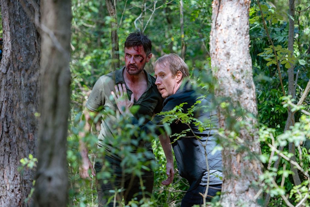 two men in woods, one covered in blood